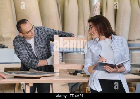 Furniture joinery production, working male joiner and female business owner with notebook in woodworking workshop Stock Photo