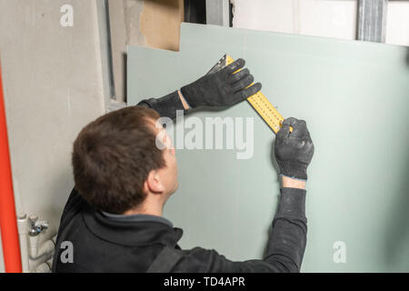 A man working Builder makes a marking on the drywall for electrical wiring. Metal drywall construction in a house during renovation. Stock Photo