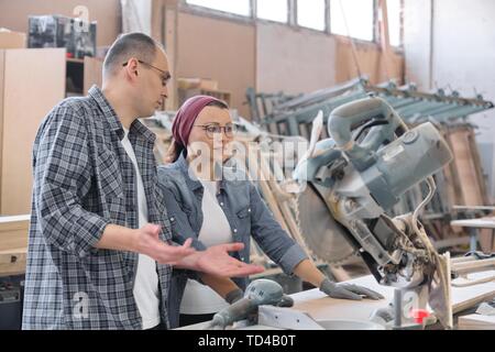 Industrial portrait of two working men and woman, talking at machine tools in workshop producing carpentry products Stock Photo