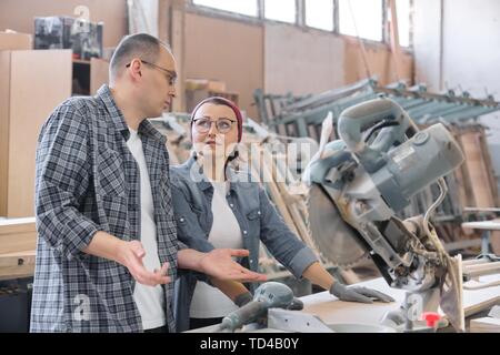 Industrial portrait of two working men and woman, talking at machine tools in workshop producing carpentry products Stock Photo