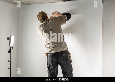 Worker applies a sheet of Wallpaper. Man glueing wallpapers on concrete  wall. Repair the apartment. Home renovation concept. White Wallpaper for  paint Stock Photo - Alamy