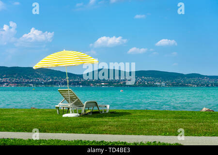 Stylish lounger plastic sunbed with yellow stripes sunshade beach umbrella on the green grass on beach at summer under open sky. Sunbed intended for Stock Photo