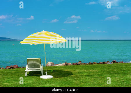 Stylish lounger plastic sunbed with yellow stripes sunshade beach umbrella on the green grass on beach at summer under open sky. Sunbed intended for Stock Photo