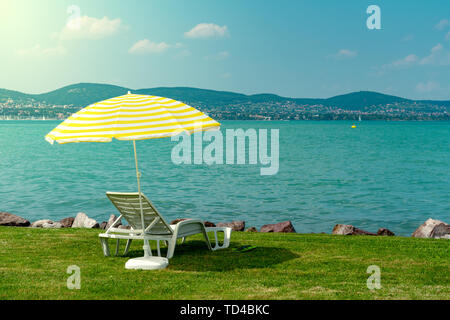 Stylish lounger plastic sunbed with yellow stripes sunshade beach umbrella on the green grass on beach at summer under open sky. Sunbed intended for Stock Photo