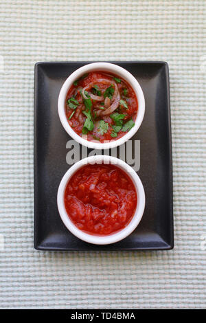 Tomato sauce or marinade for meat and bbq with onion and herbs. Ceramic white bowls and rectangular dark gray plate Stock Photo