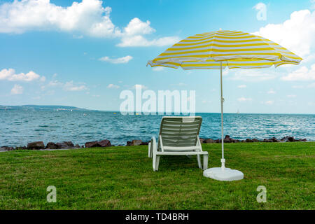 Stylish lounger plastic sunbed with yellow stripes sunshade beach umbrella on the green grass on beach at summer under open sky. Sunbed intended for Stock Photo