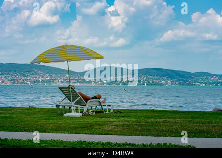 Stylish lounger plastic sunbed with yellow stripes sunshade beach umbrella on the green grass on beach at summer under open sky. man sunbathing on the Stock Photo