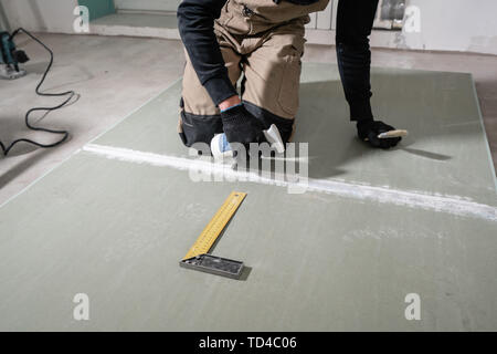 Worker is using a polyurethane foam for gluing drywall at ninety degrees. Hand holding polyurethane expanding foam glue gun applicator Stock Photo