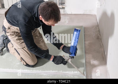 Worker is using a polyurethane foam for gluing drywall at ninety degrees. Hand holding polyurethane expanding foam glue gun applicator Stock Photo