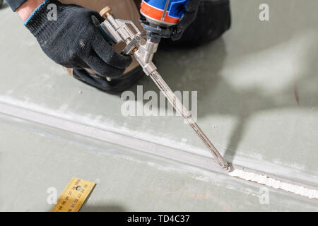Worker is using a polyurethane foam for gluing drywall at ninety degrees. Hand holding polyurethane expanding foam glue gun applicator Stock Photo