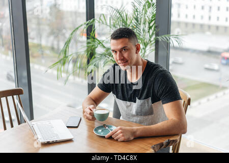 Young man drinking coffee from a Cup. Freelancer work on netbook in modern coworking. Programmer at remote job. Successful people, businessman in Stock Photo
