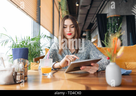 Female smile. Young woman Typing on tablet, chatting, maintains a blog. Freelancer work in cafe modern coworking. Successful people, businessman in Stock Photo