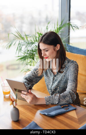 Female smile. Young woman Typing on tablet, chatting, maintains a blog. Freelancer work in cafe modern coworking. Successful people, businessman in Stock Photo