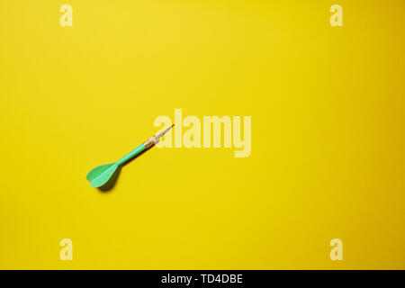 Single green arrow dart isolated on yellow background Stock Photo