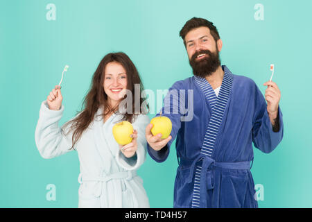 Couple in love cleaning teeth. Freshness and cleanliness. Keep teeth healthy. Healthy habits. Brush teeth every morning. Oral hygiene. Couple bathrobes hold toothbrushes and apples. Personal hygiene. Stock Photo