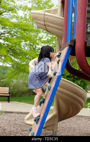 Cute little girl is climbing up on ladder in playground Stock Photo