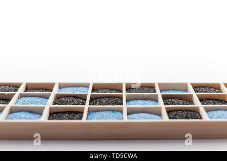 Low angle view of a rectangular wooden box with square compartments filled with black and blue decorative sand against white background. Stock Photo