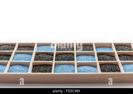 Low angle view of a rectangular wooden box with square compartments filled with black and blue decorative sand against white background. Stock Photo