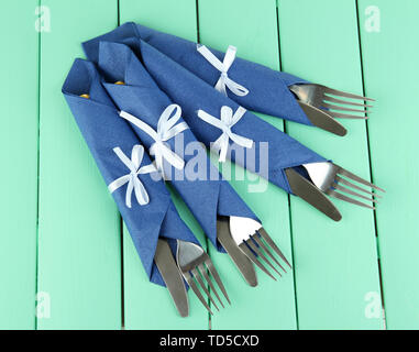 Forks and knives wrapped in blue paper napkins, on color wooden background Stock Photo