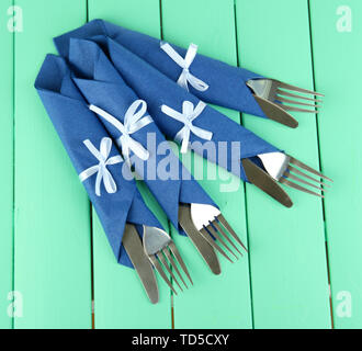 Forks and knives wrapped in blue paper napkins, on color wooden background Stock Photo