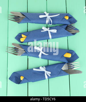 Forks and knives wrapped in blue paper napkins, on color wooden background Stock Photo