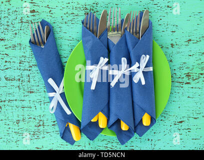 Forks and knives wrapped in blue paper napkins, on color wooden background Stock Photo