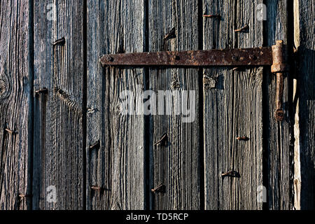 Detail of an old wooden barn door in the rural Finland. The old iron hinge still keeps the barn door closed. Stock Photo