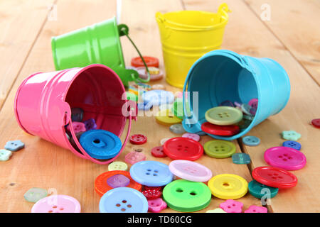 Colorful buttons strewn from buckets on wooden background Stock Photo