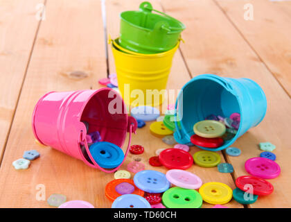 Colorful buttons strewn from buckets on wooden background Stock Photo