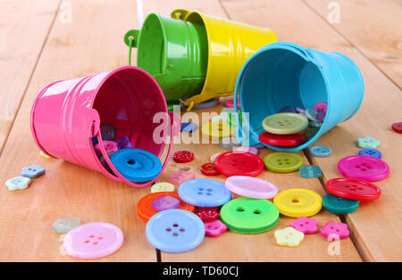 Colorful buttons strewn from buckets on wooden background Stock Photo
