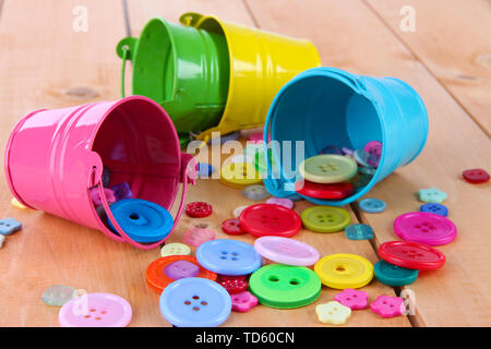 Colorful buttons strewn from buckets on wooden background Stock Photo