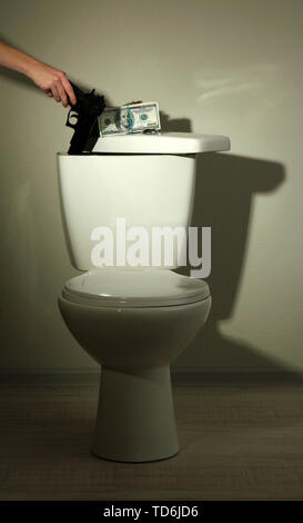 Hand hides gun and money in toilet tank in a bathroom Stock Photo