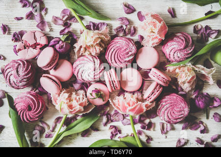 Flat-lay of macaron cookies, marshmallows and flowers over wooden background Stock Photo