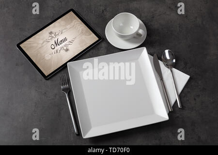 Tablet with stylish restaurant logo and laid table  Stock Photo