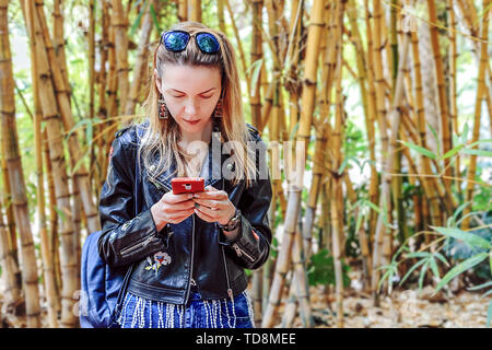 A girl with blond hair is looking at something in the phone while standing directly to the camera with her head bent. Morocco Stock Photo