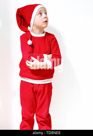 A little boy in the shape of a Santa Claus is smiling, stands on a white background, and looks up Stock Photo