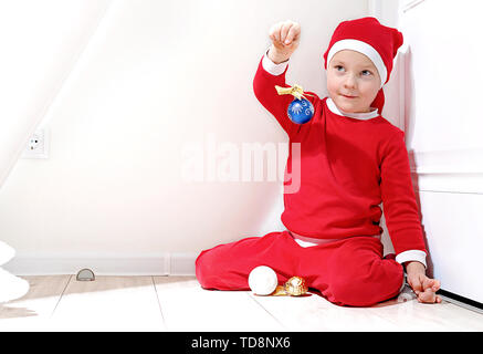 A little boy in the shape of Santa Claus is smiling, stands on a white background, and holds a Christmas toy in his hand Stock Photo