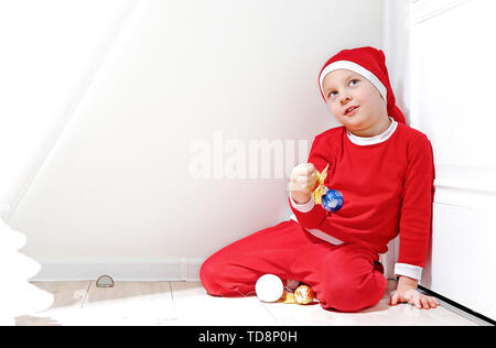 A little boy in the shape of Santa Claus is smiling, stands on a white background, and holds a Christmas toy in his hand Stock Photo