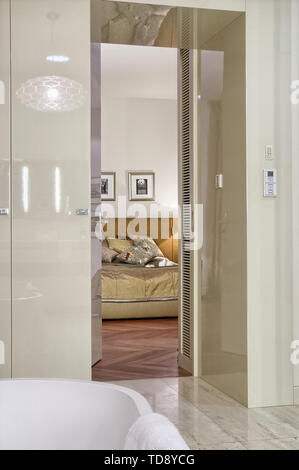 Passage from bathroom to spacious bedroom with comfortable double bed with wicker headboard  UK & IRISH USE ONLY Stock Photo