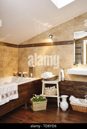 White rolled-up towels in wicker basket on stool next to tiled bathtub in bathroom  UK & IRISH USE ONLY Stock Photo