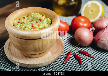 fresh guacamole in a wood bowl next to ingredients, typical mexican healthy vegan cuisine with rustic dark food photo style Stock Photo