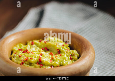 homemade guacamole in a wood bowl and a kitchen rag on a wooden table, typical mexican healthy vegan cuisine Stock Photo