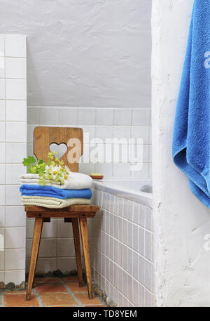 Folded towels on wooden chair in white bathroom with tiled walls  UK & IRISH USE ONLY Stock Photo