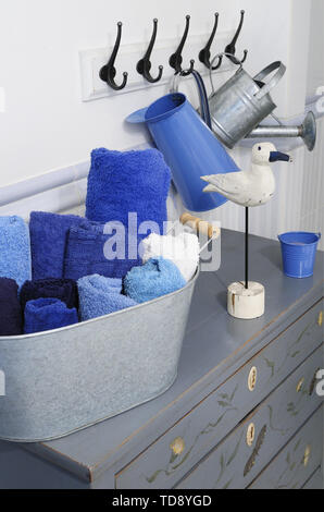 Rolled blue towels in metal basket on chest of drawers in bathroom   UK & IRISH USE ONLY Stock Photo