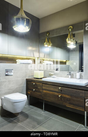 Large yellow square candle on wooden countertop next to washbasin in modern bathroom   UK & IRISH USE ONLY Stock Photo