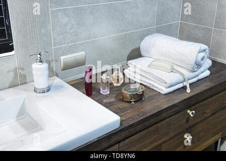 White towels and perfumes on wooden countertop next to washbasin in modern bathroom   UK & IRISH USE ONLY Stock Photo