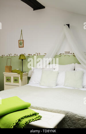 Green folded blanket on bench in front of comfortable double bed with pillows and net curtain in attic bedroom    UK AND IRISH RIGHTS ONLY Stock Photo