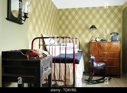 Dark brown rustic wooden rocking horse next to rustic metal bed in teen boy bedroom   UK & IRISH USE ONLY Stock Photo
