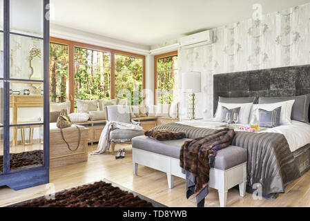 Faux fur blanket on sitting bench next to comfortable double bed with padded headboard in attic bedroom    UK AND IRISH RIGHTS ONLY Stock Photo