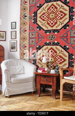 Two armchairs and oriental coffee table next to decorative rug on wall in living room    UK AND IRISH RIGHTS ONLY Stock Photo